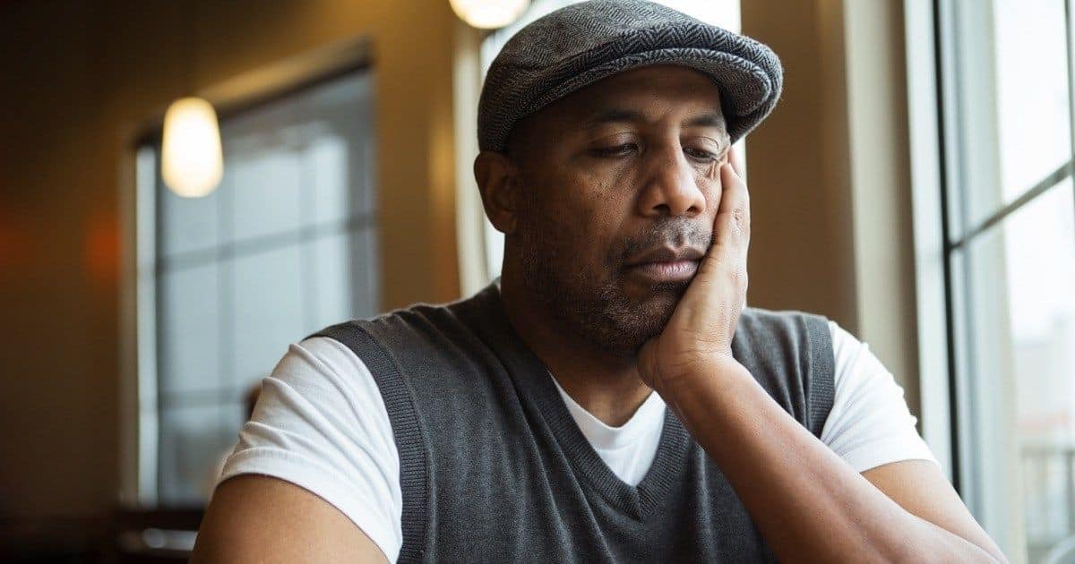 Man sitting by a window with his head in his hand