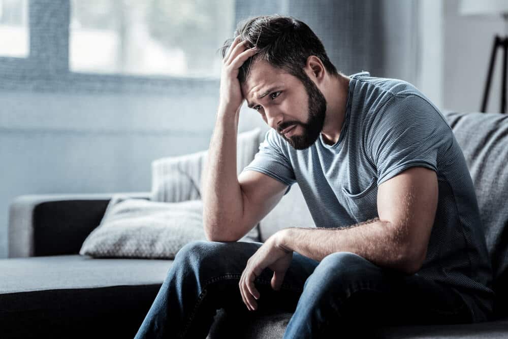 A depressed man sitting on a couch with his hand on his head