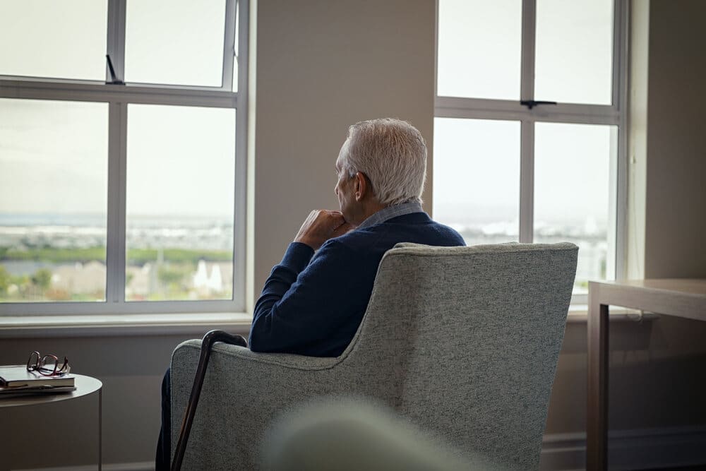 An older man sitting in the dark and looking out the window