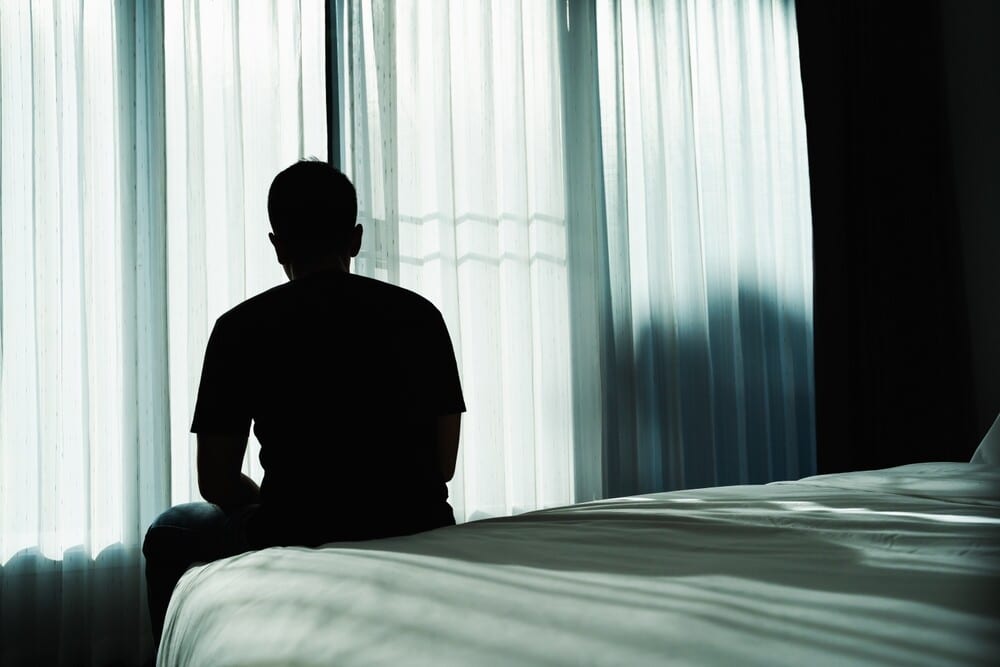 A depressed man sitting on the edge of his bed