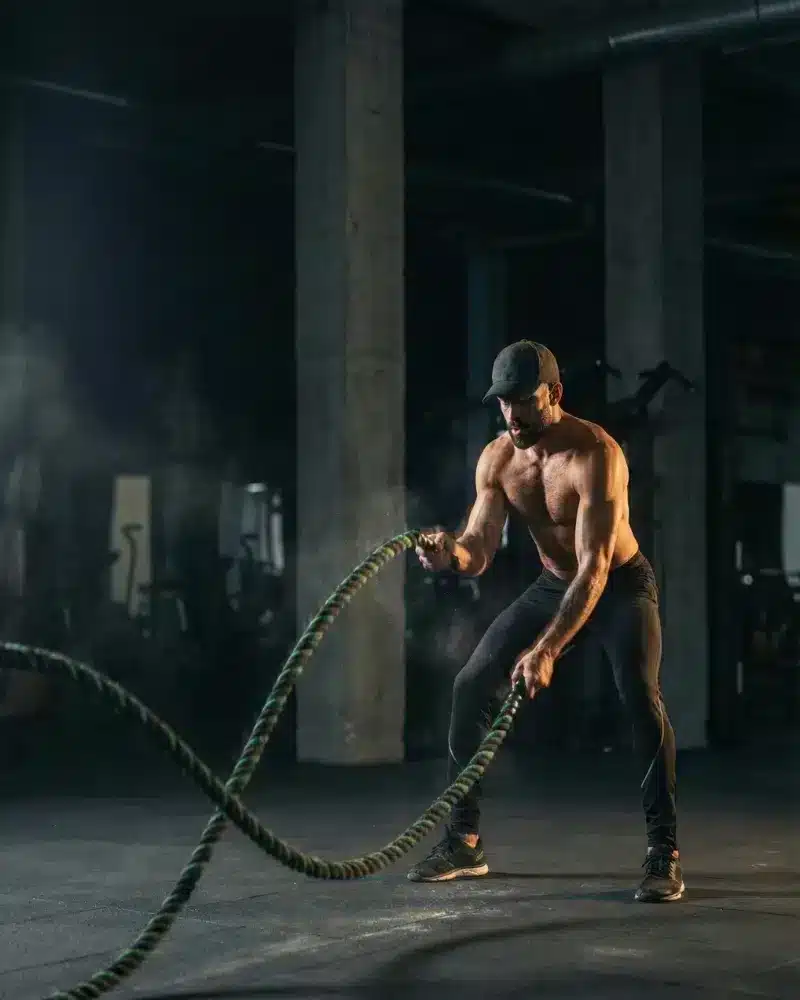 A man in athletic wear using battle ropes with explosive motion, demonstrating physical vitality.